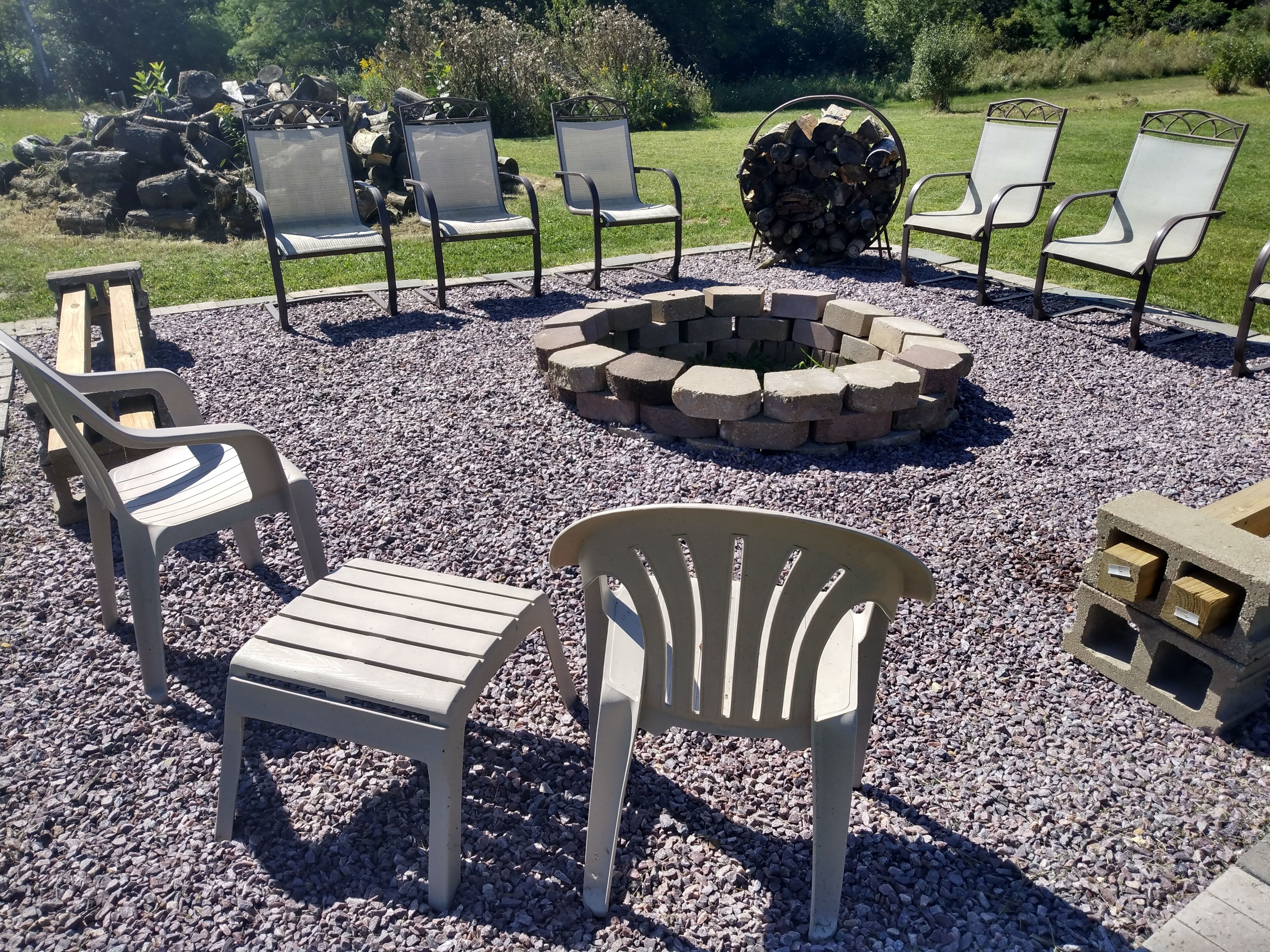 An outdoor seating area with a fire pit, surrounded by chairs and a table, set on gravel.