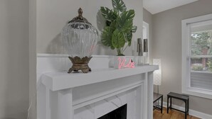 A modern living room with a white fireplace, a decorative glass vase, a large green plant, and a neon sign that reads "Vibe". - The Vibe at OSU: Walking distance to the stadium! (Columbus)