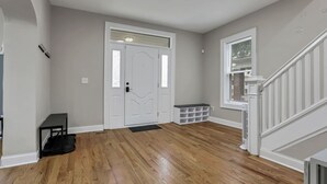 A spacious hallway with hardwood flooring, a white door with a vent, a small table, and a bench with storage compartments. - The Vibe at OSU: Walking distance to the stadium! (Columbus)