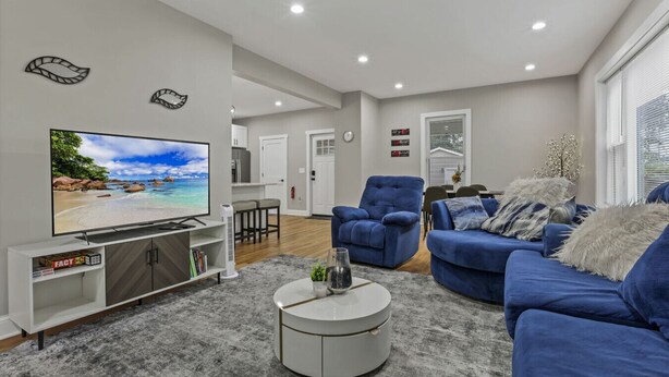 A modern living room with a flat-screen TV, blue sofas, a coffee table, and a dining area in the background. - The Vibe at OSU: Walking distance to the stadium! (Columbus)
