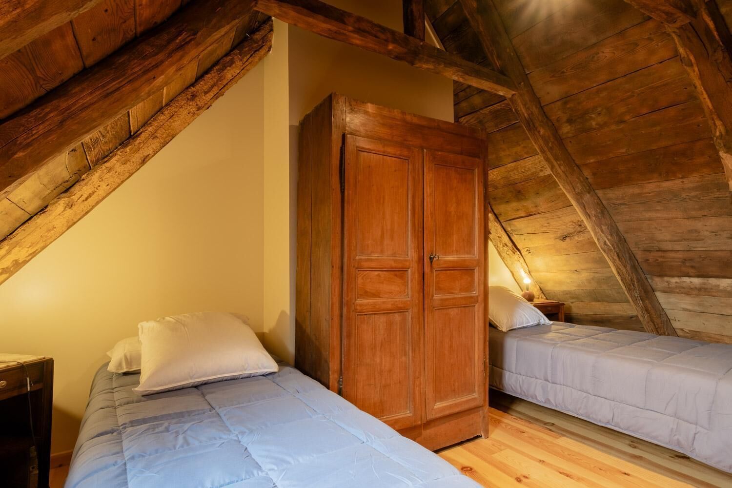 A bedroom with two beds, wooden beams, and a large wardrobe.