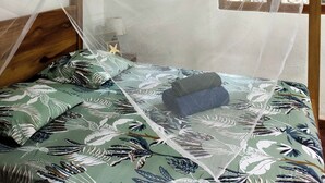 A room with a bed under a mosquito net, a window with a view of greenery, and wooden beams on the ceiling. - FINCA ARDILLA (Cahuita)