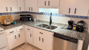 A kitchen with white cabinets, a double sink, a microwave, a coffee maker, and a dishwasher.