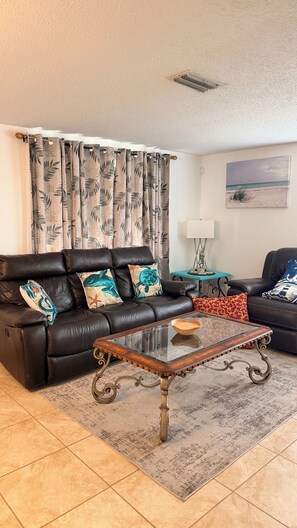 A living room with a leather sofa, a glass coffee table, and a patterned rug.