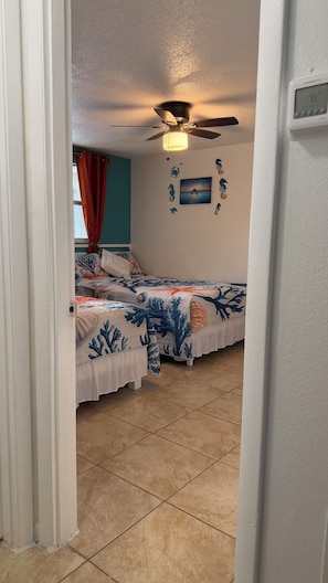 Un dormitorio con dos camas, ventilador de techo y termostato en la pared.
