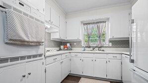 A modern kitchen with white cabinets, a built-in oven, a window with curtains, and a wooden floor.