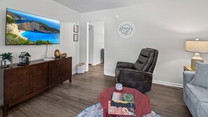 A living room with a flat-screen TV, a leather chair, a sofa, a coffee table, and a cabinet.