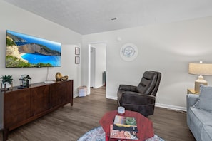 A living room with a flat-screen TV, a leather chair, a sofa, a coffee table, and a cabinet.