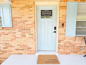 A light blue door with a window, a doormat with text, and a brick wall. - Hailey's Retreat- 3/2 Cozy & Spacious Home + Sunroom- 6 min to Downtown Dothan! (Dothan)