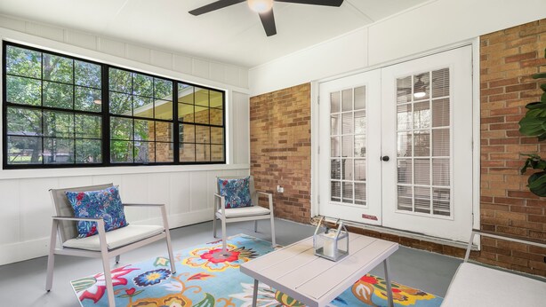 A room with a large window, two chairs, a table, and a colorful floral rug.