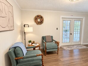 A room with two green armchairs, a floor lamp, a small table with a plant, and a door with a window. - Hailey's Retreat- 3/2 Cozy & Spacious Home + Sunroom- 6 min to Downtown Dothan! (Dothan)