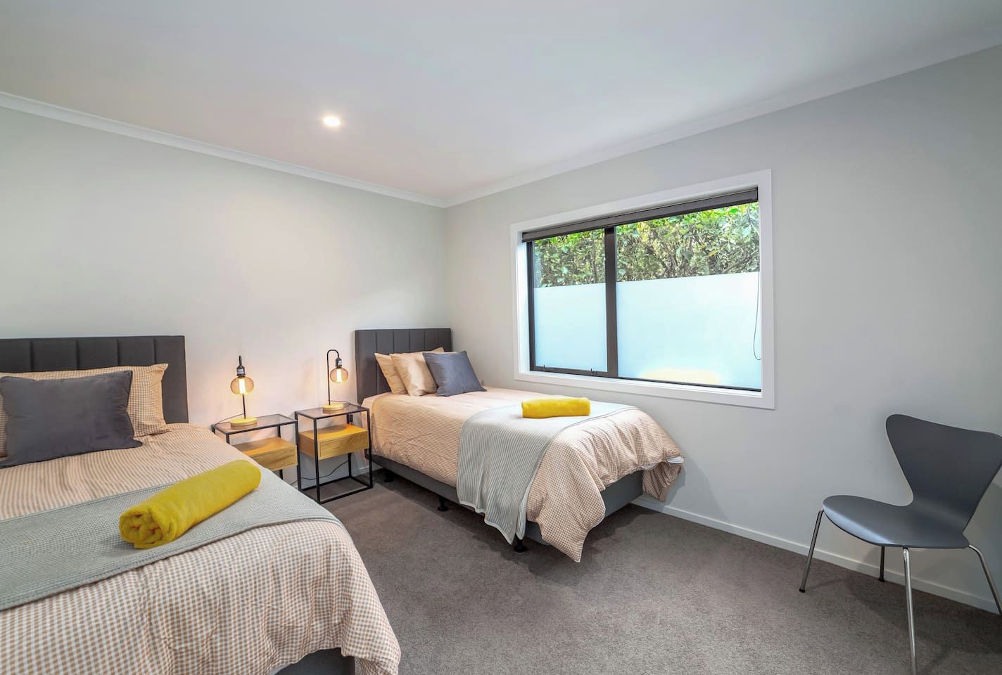 Une chambre moderne avec deux lits, une grande fenêtre et un fauteuil.