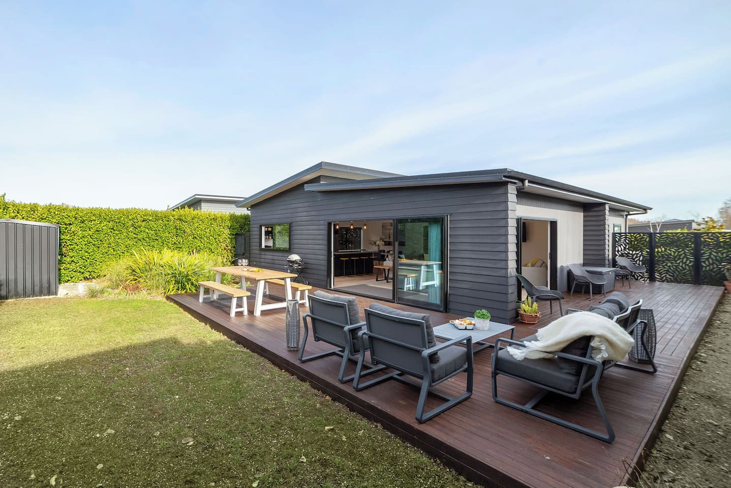 Une maison moderne dotée d’une terrasse, d’un espace salon extérieur et d’un coin cuisine.