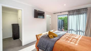 A bedroom with a bed, a TV mounted on the wall, a closet, and a view of greenery outside.