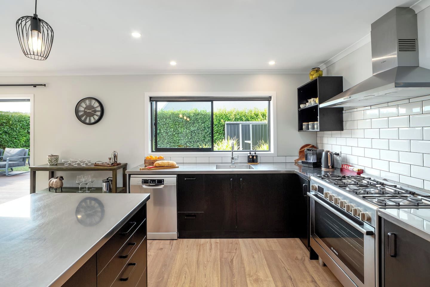 A modern kitchen with a large island, stainless steel appliances, and a view of greenery outside.