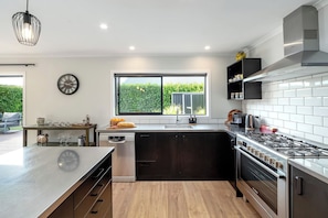 A modern kitchen with a large island, stainless steel appliances, and a view of greenery outside.
