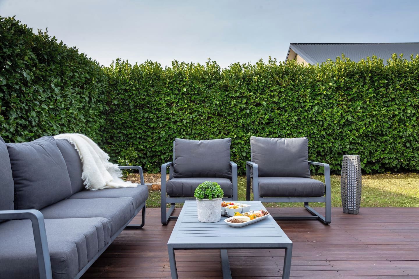 Un espacio exterior con asientos al aire libre, que incluye un sofá, dos sillones y una mesa, todo con cojines grises.