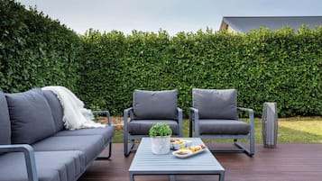 Un espacio exterior con asientos al aire libre, que incluye un sofá, dos sillones y una mesa, todo con cojines grises.
