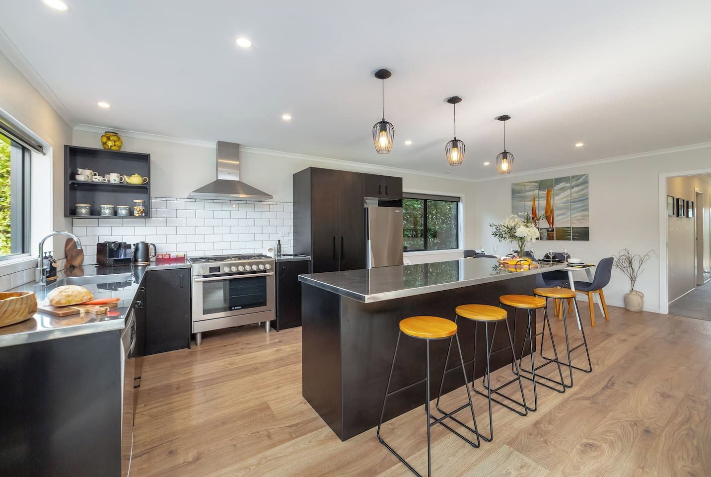 A modern kitchen with a central island, bar stools, and a dining area with a view.