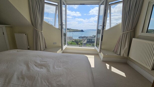 A bedroom with a large bed, a view of the sea, and a window with curtains. - Highlands - sleeps 7 guests  in 4 bedrooms (St Mawes)