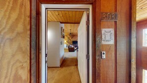 Un pasillo interior de madera que conduce a una sala de estar con ventilador de techo, un sofá y un televisor.