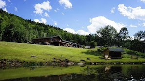 A lodge with a large building and a smaller cabin, surrounded by a grassy area and a pond.