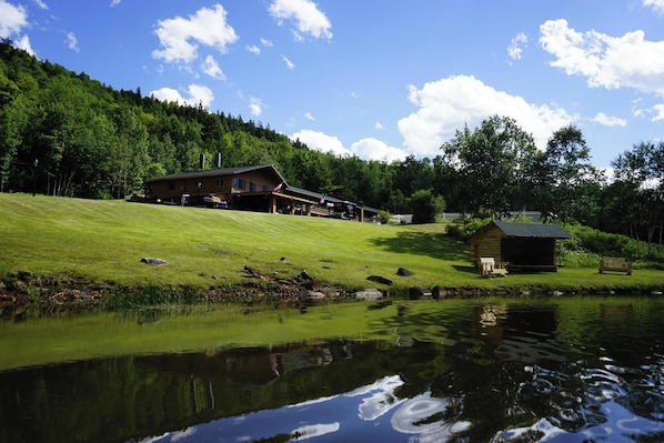 A lodge with a large building and a smaller cabin, surrounded by a grassy area and a pond. - Ledgerock at Whiteface - Queen Room (Wilmington)