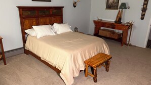 A bedroom with a wooden bed, a bedside table, a nightstand, a desk with a lamp, and wall-mounted decor.