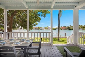A covered outdoor area with a table set for dining, overlooking a body of water and buildings. - Lovely Water View! 3 Bed, 3 BA Townhome, Cabana Club: Oceanfront Beach, Pool! (Marathon)