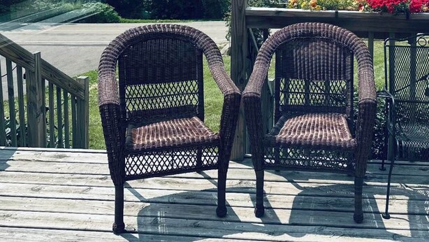 A wooden deck with wicker chairs facing a lake view.