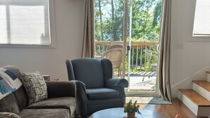 A living room with a sofa, armchair, and coffee table. There is a sliding glass door leading to an outdoor area with a wooden deck.