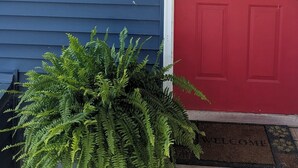 A red door with a 'Welcome' sign, a potted plant, and a white lantern on a blue siding house.