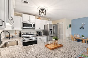 A modern kitchen with white cabinets, stainless steel appliances, granite countertops, and a dining area with wooden chairs.