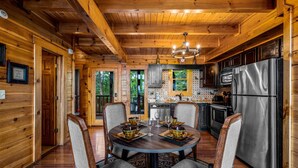 A wooden cabin interior with a dining table set for four, surrounded by chairs, and a kitchen area with modern appliances. - Romantic Lookout | Incredible Views - Hot Tub - Pool Table (Sevierville)