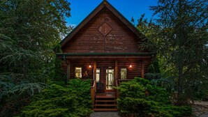 A wooden cabin with a porch, surrounded by dense greenery. - Romantic Lookout | Incredible Views - Hot Tub - Pool Table (Sevierville)