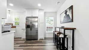 A modern kitchen with white cabinetry, a stainless steel refrigerator, and a bar area with stools. - Boots & Bedrolls - Walkable to Fort Worth's Dickies Arena. (Fort Worth)