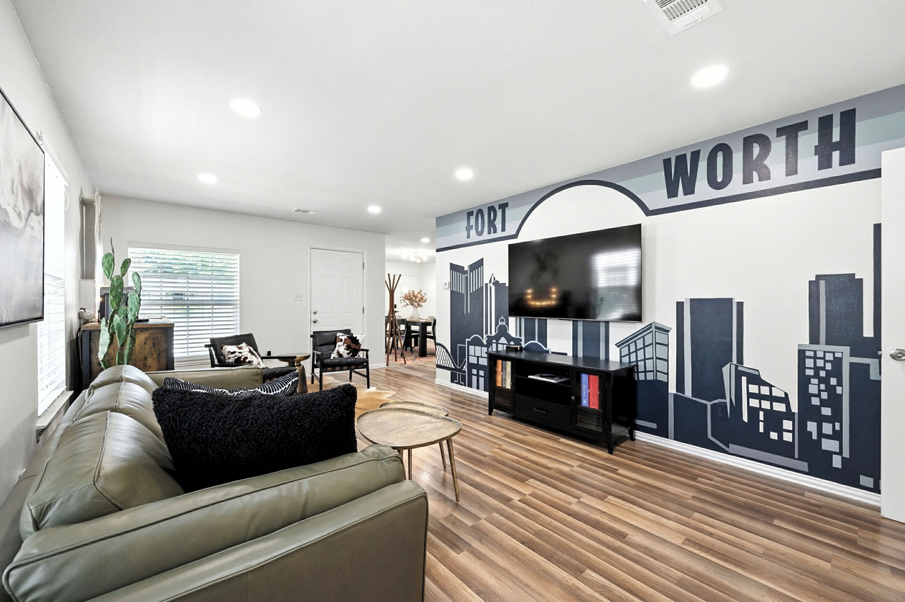 Un salon moderne avec une fresque représentant un paysage urbain, un canapé en cuir, un téléviseur et un plancher en bois.