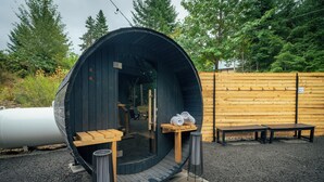 A large, dark wooden sauna with benches and a table, surrounded by a wooden fence and trees. - Packwood: Chalet + Nest (Packwood)