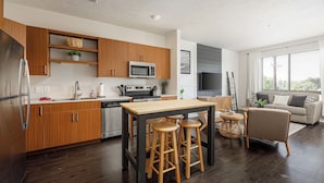 A modern kitchen with wooden cabinets, a stainless steel refrigerator, and a central island with stools.