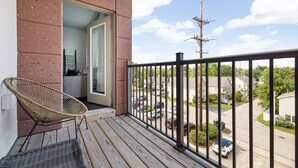 A balcony with a wicker chair, a view of a residential street, and a utility pole.