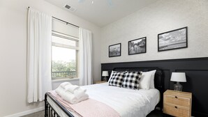 A neatly made bed with white linens and a pink throw, a bedside table with a lamp, and a wall with three framed pictures.