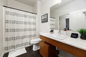 Une salle de bain moderne avec des toilettes blanches, un meuble-lavabo en bois, un lavabo et un rideau de douche.