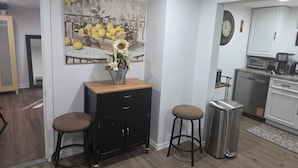 A kitchen with a sink, stove, and cabinets. There is a painting on the wall and a trash can.