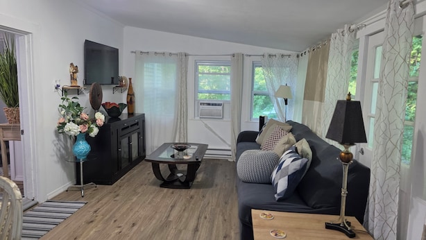 A modern living room with a sofa, coffee table, and decorative items. There is a television on a stand, a window with curtains, and a lamp on a side table.