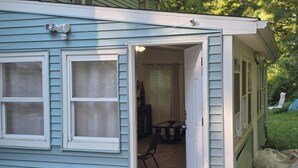 A small, light blue building with a door open to a porch area.