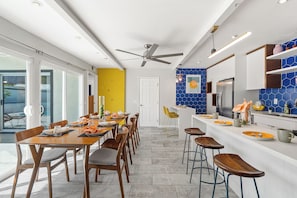 Cozinha moderna com área de jantar, apresentando uma mesa grande, cadeiras, geladeira e painel de azulejos azuis.