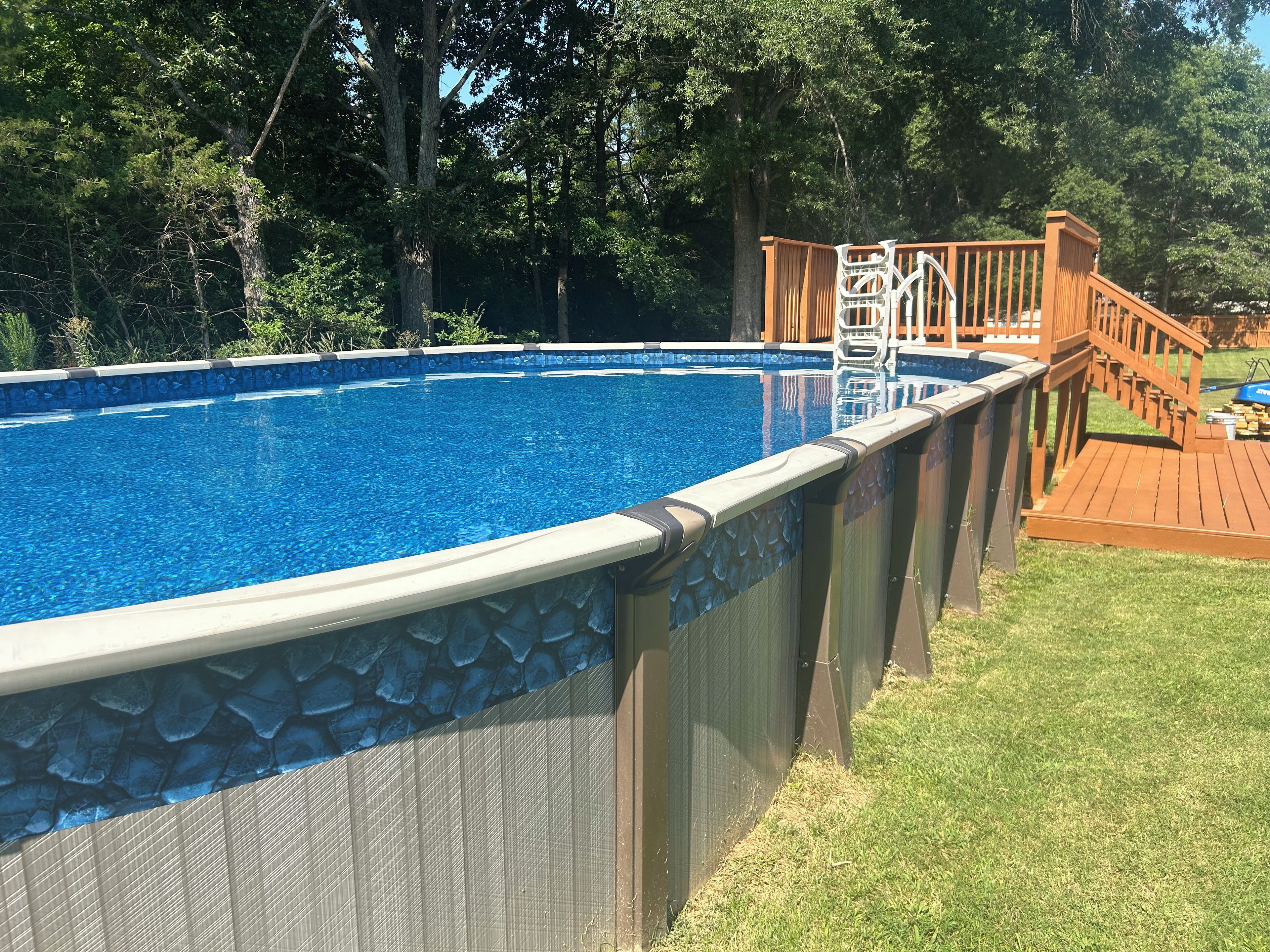 An above-ground swimming pool with a wooden deck and a ladder.
