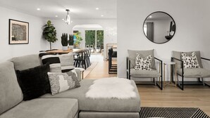 A modern living room with a grey sectional sofa, a round mirror, and a dining area with chairs and a table.