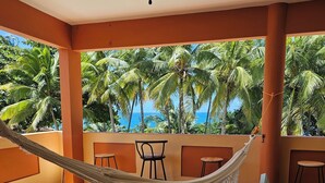 Una hamaca sobre suelo de baldosas, con vista a palmeras y al océano.