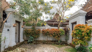 A courtyard with stone paving, white brick walls, and various plants. - Sakya Villa (Canggu)